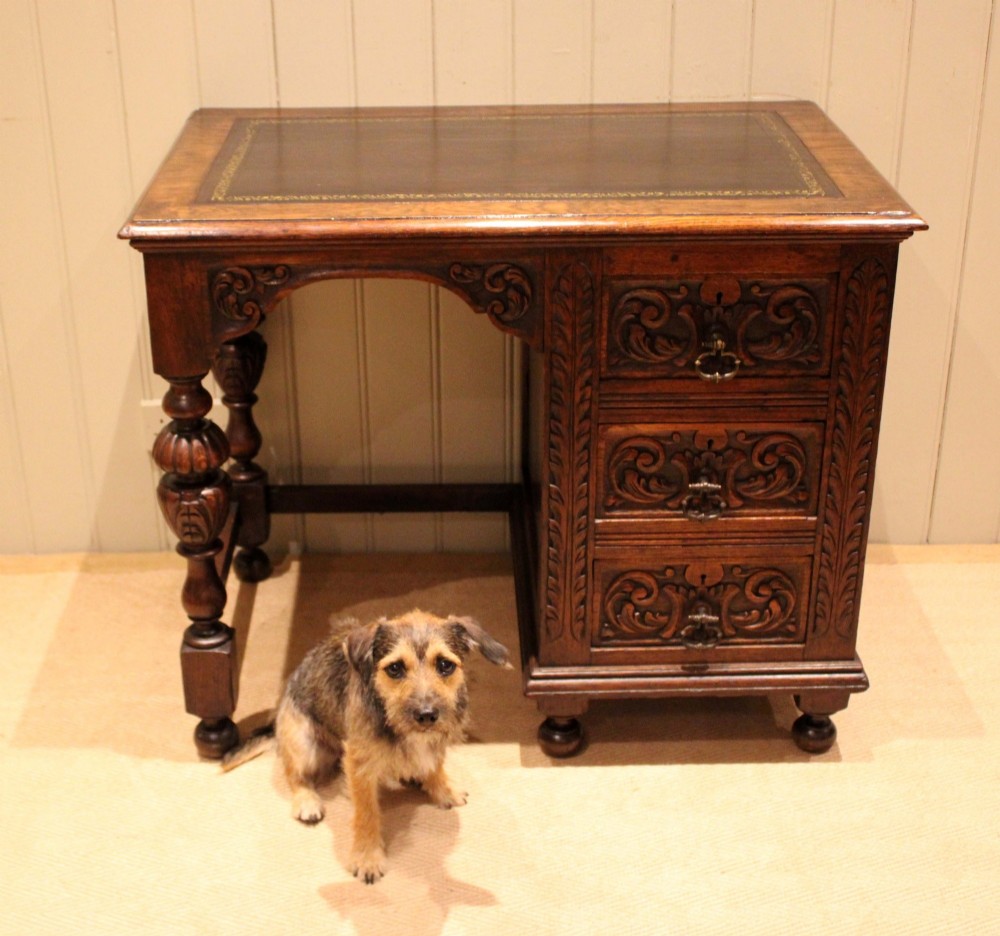 A late nineteenth-century dark carved oak writing desk featuring three side drawers with detailed foliate carvings and a leather inset writing surface. View X