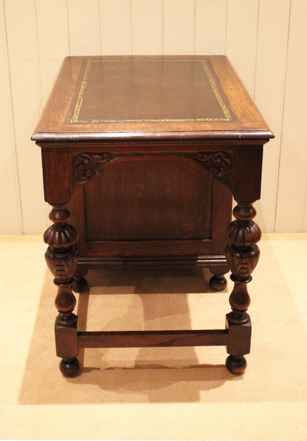 A late nineteenth-century dark carved oak writing desk featuring three side drawers with detailed foliate carvings and a leather inset writing surface. View XI