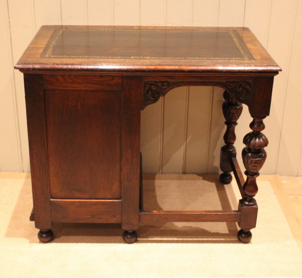 A late nineteenth-century dark carved oak writing desk featuring three side drawers with detailed foliate carvings and a leather inset writing surface. View XII