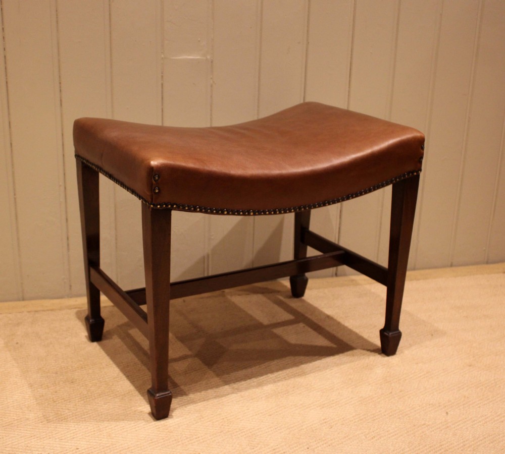 An Edwardian mahogany stool featuring a concave tan leather seat trimmed with brass studs and supported by square tapered legs with stretchers. View VIII