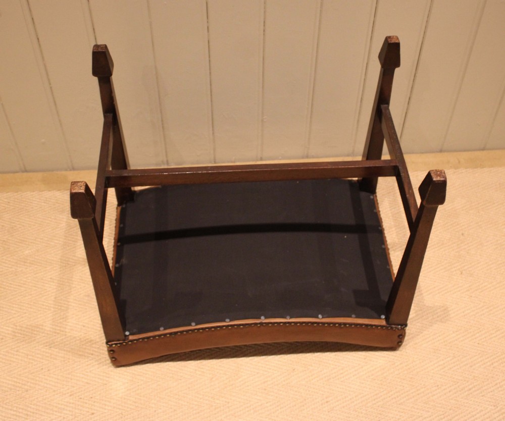 An Edwardian mahogany stool featuring a concave tan leather seat trimmed with brass studs and supported by square tapered legs with stretchers. View XIII