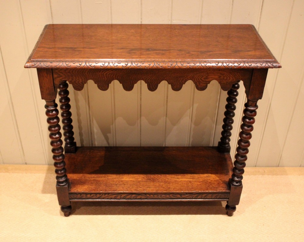 A dark oak console table featuring a rectangular top with carved moulding, a scalloped apron, four bobbin-turned legs, and a lower tier shelf.