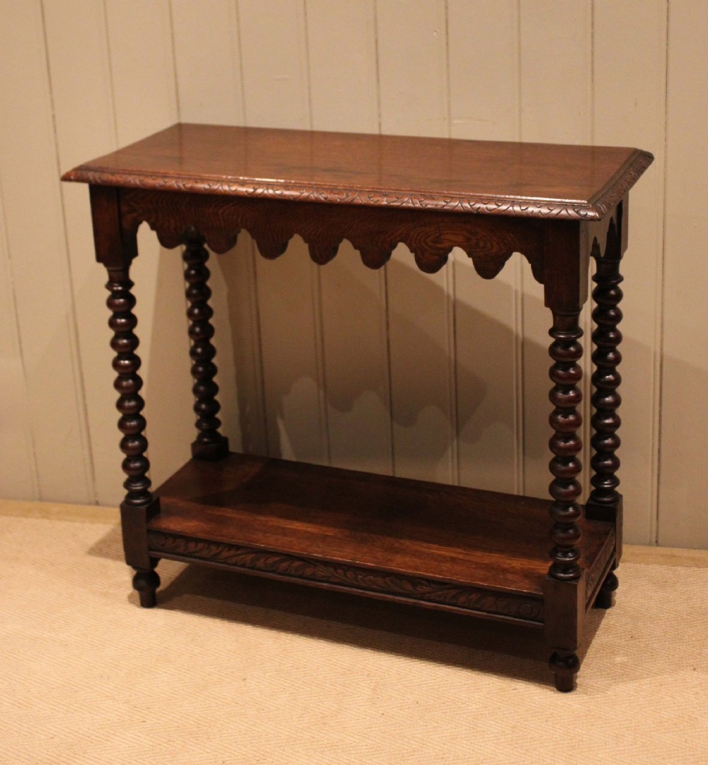 A dark oak console table featuring a rectangular top with carved moulding, a scalloped apron, four bobbin-turned legs, and a lower tier shelf. View V