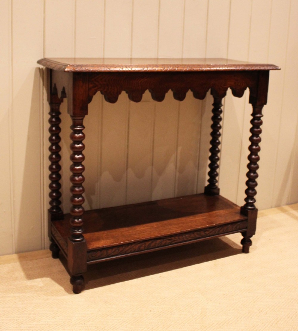 A dark oak console table featuring a rectangular top with carved moulding, a scalloped apron, four bobbin-turned legs, and a lower tier shelf. View VI