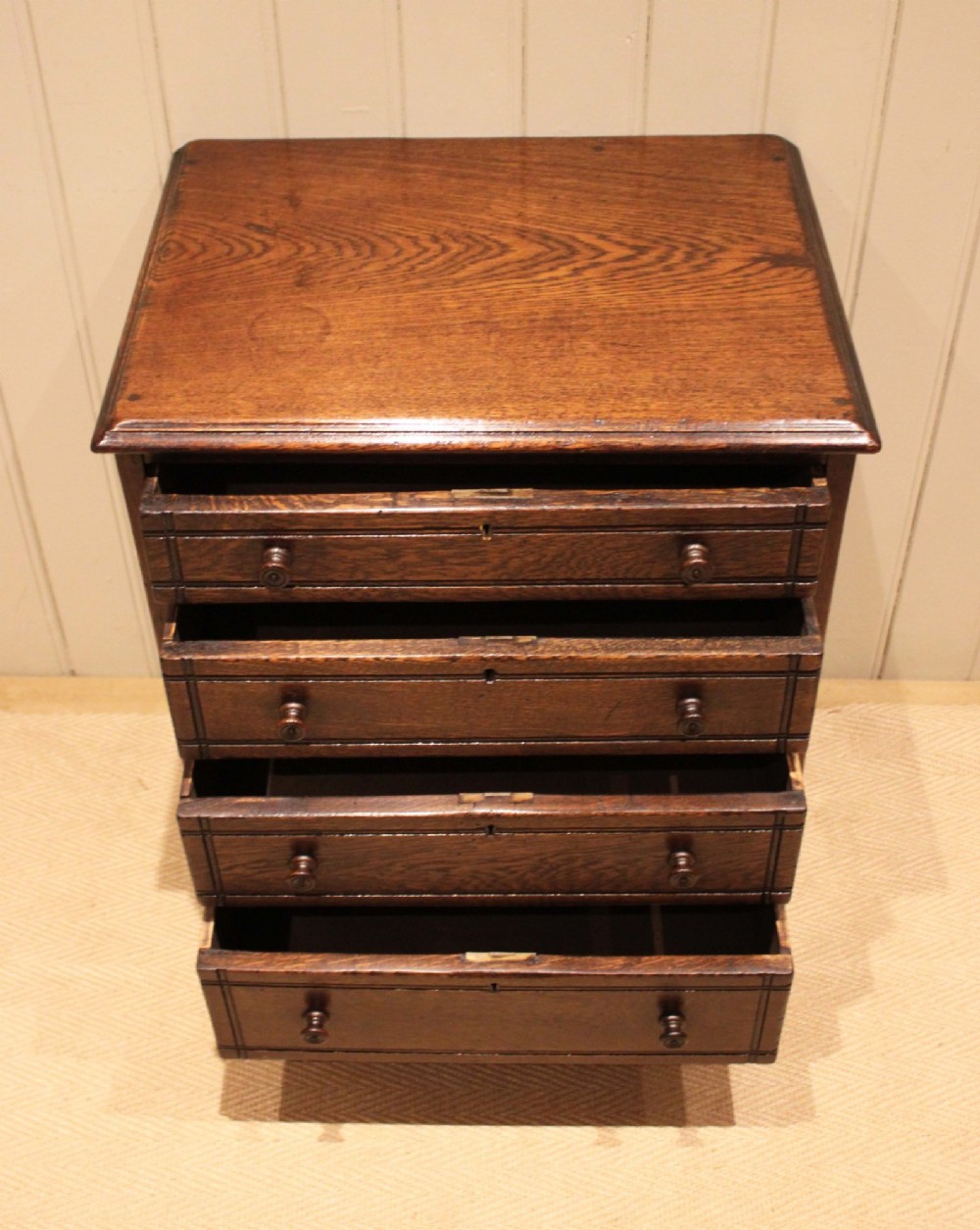 A small solid oak chest of four drawers featuring turned wooden knobs and incised border detailing. View V