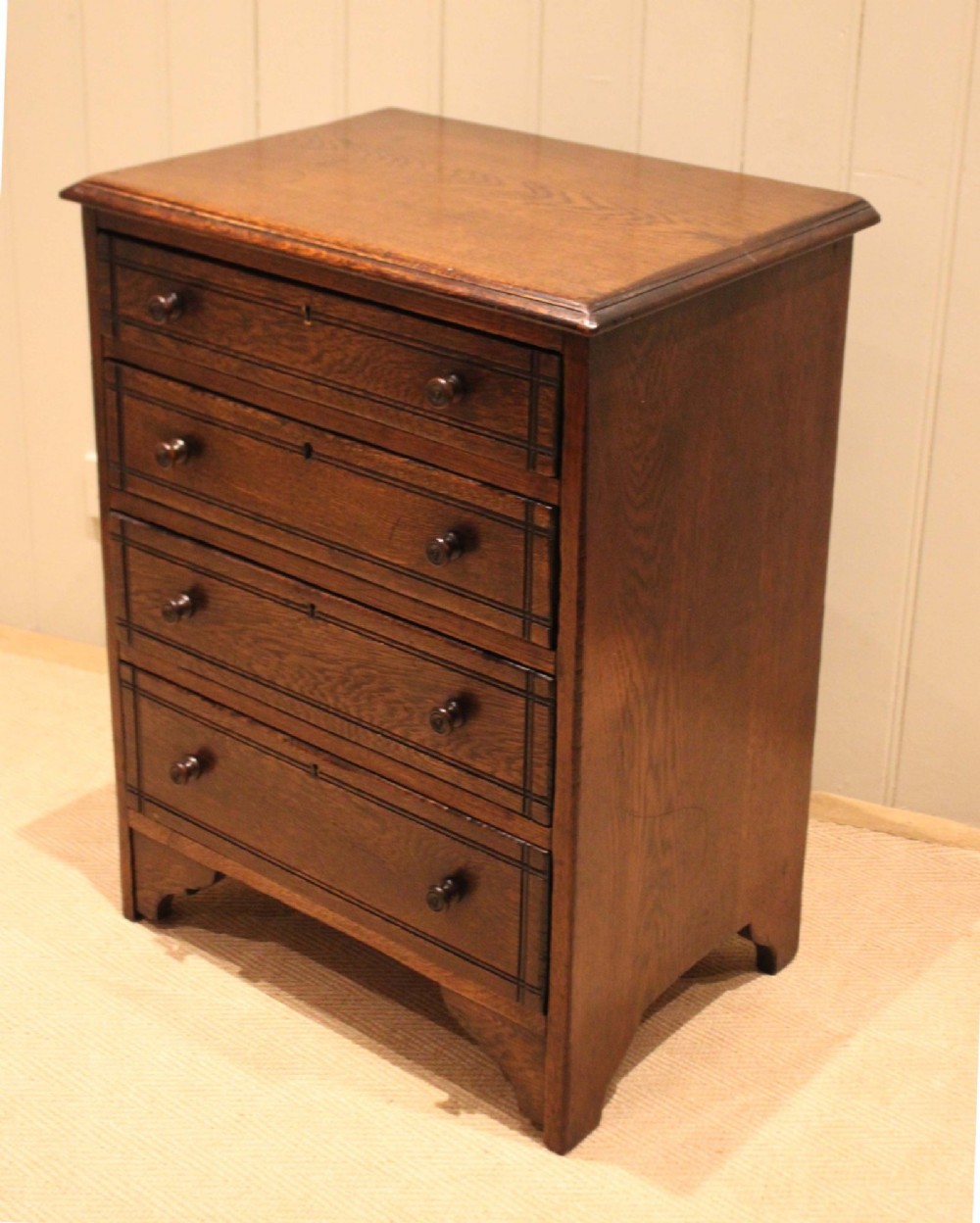 A small solid oak chest of four drawers featuring turned wooden knobs and incised border detailing. View VI