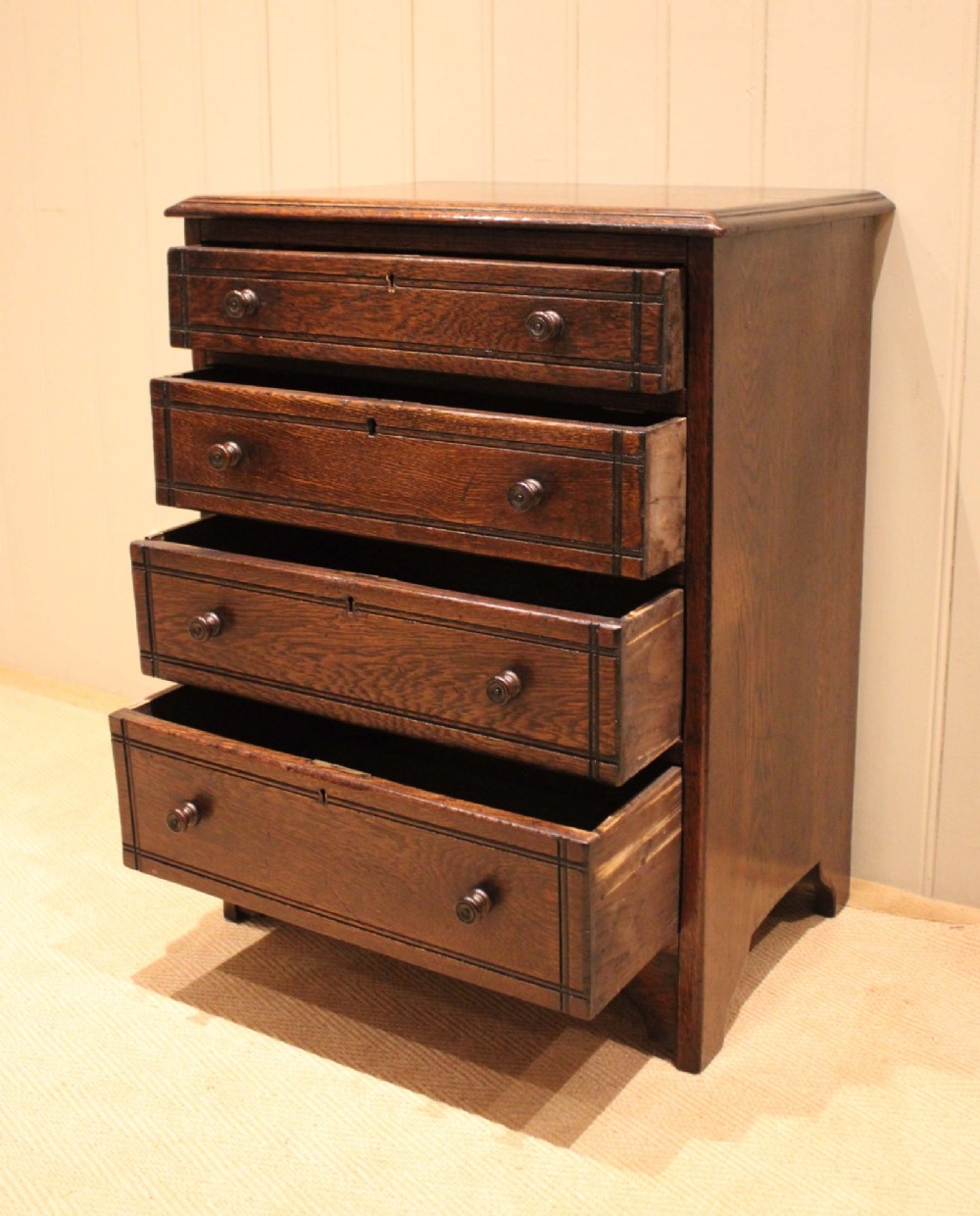 A small solid oak chest of four drawers featuring turned wooden knobs and incised border detailing. View VII