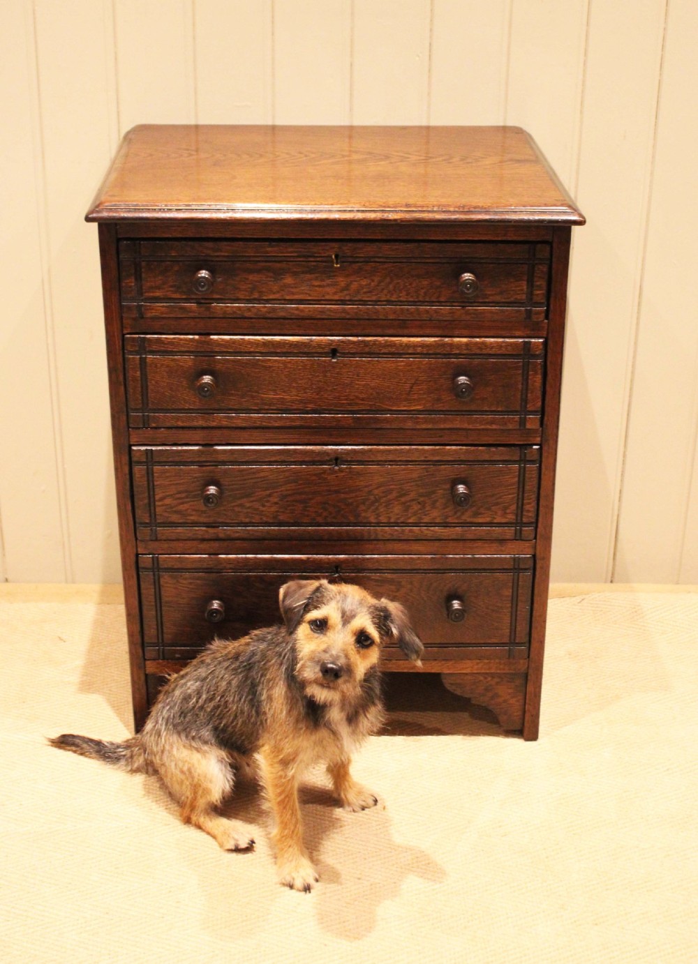 A small solid oak chest of four drawers featuring turned wooden knobs and incised border detailing. View X