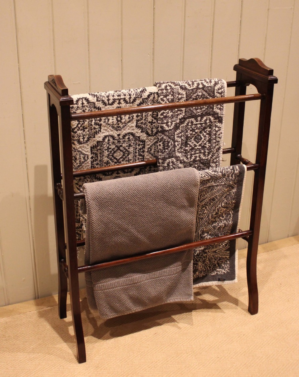 An Edwardian freestanding dark mahogany towel rail featuring six turned horizontal bars and splayed legs. View II