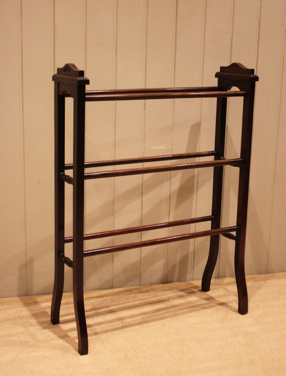 An Edwardian freestanding dark mahogany towel rail featuring six turned horizontal bars and splayed legs. View III