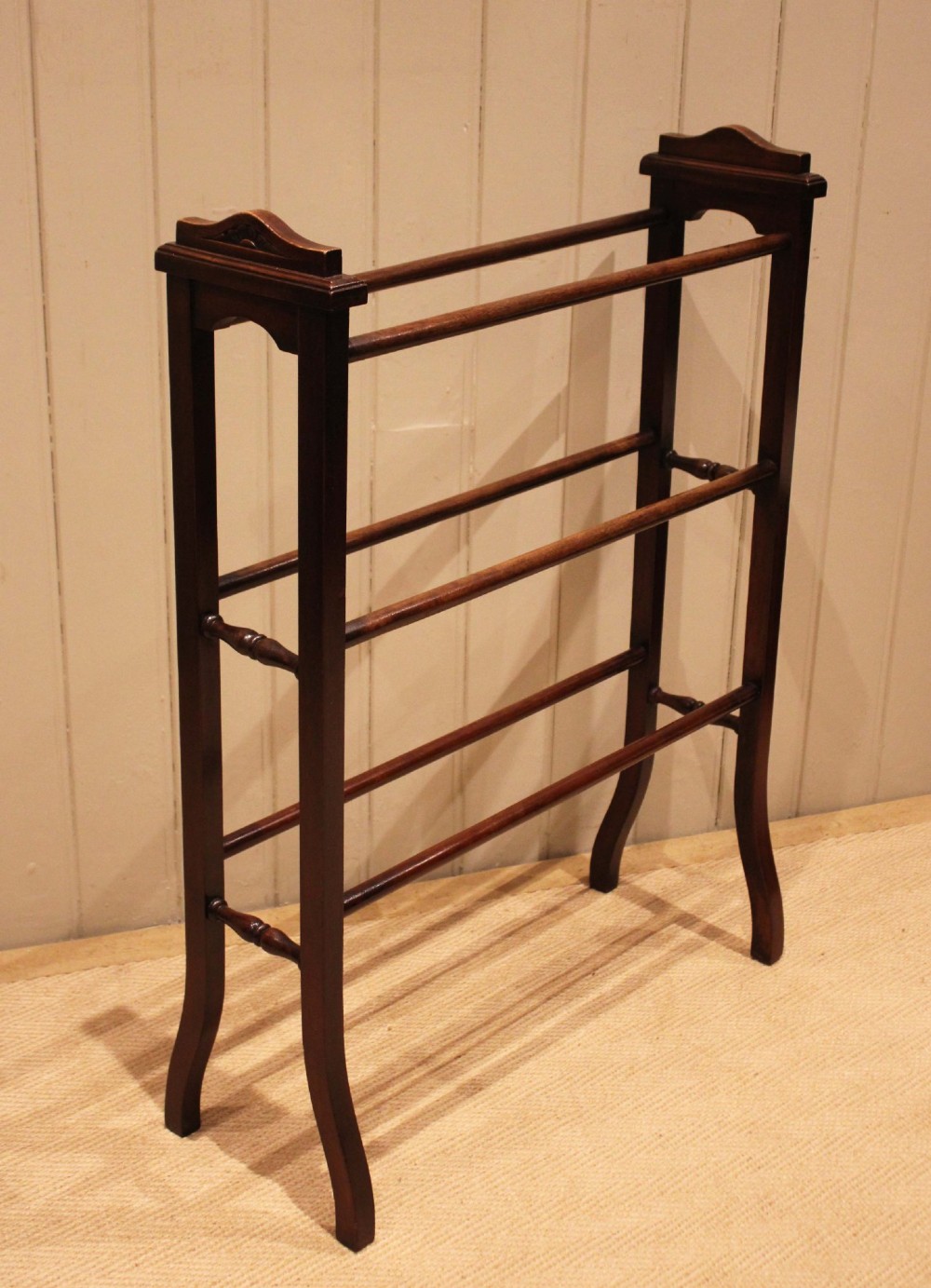 An Edwardian freestanding dark mahogany towel rail featuring six turned horizontal bars and splayed legs. View V