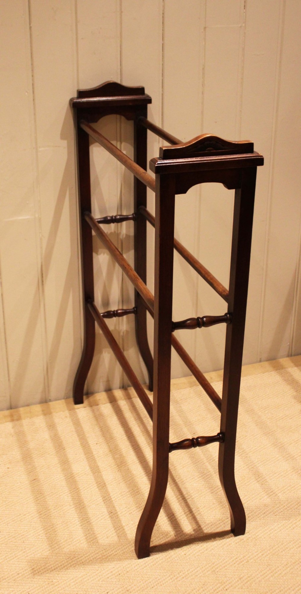 An Edwardian freestanding dark mahogany towel rail featuring six turned horizontal bars and splayed legs. View X