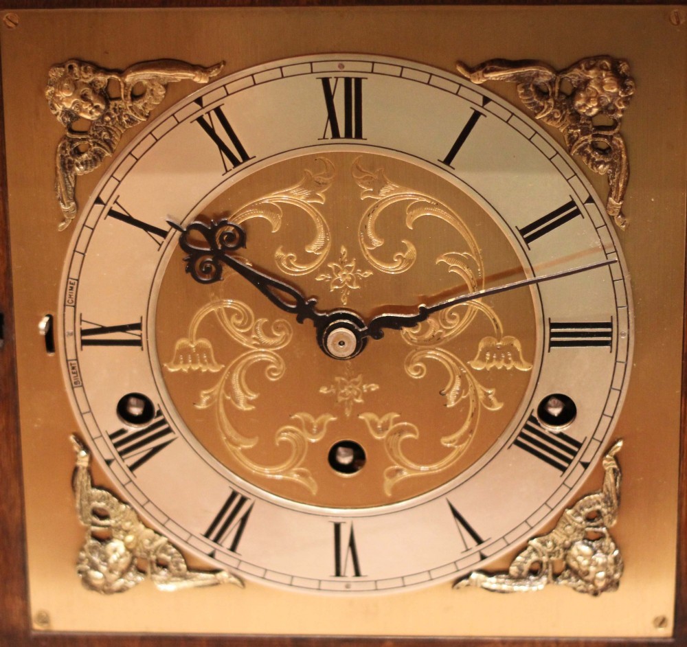 A burr walnut bracket clock featuring a caddy top with a brass carry handle, an ornate brass dial with a silvered chapter ring, and brass bracket feet. View VII
