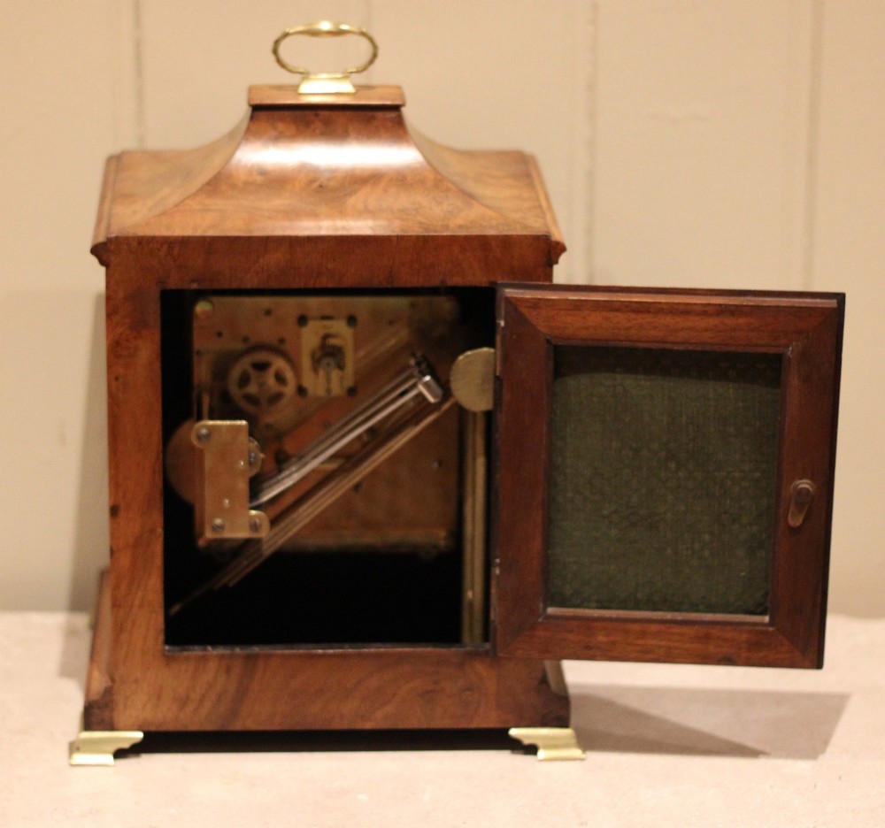A burr walnut bracket clock featuring a caddy top with a brass carry handle, an ornate brass dial with a silvered chapter ring, and brass bracket feet. View IX
