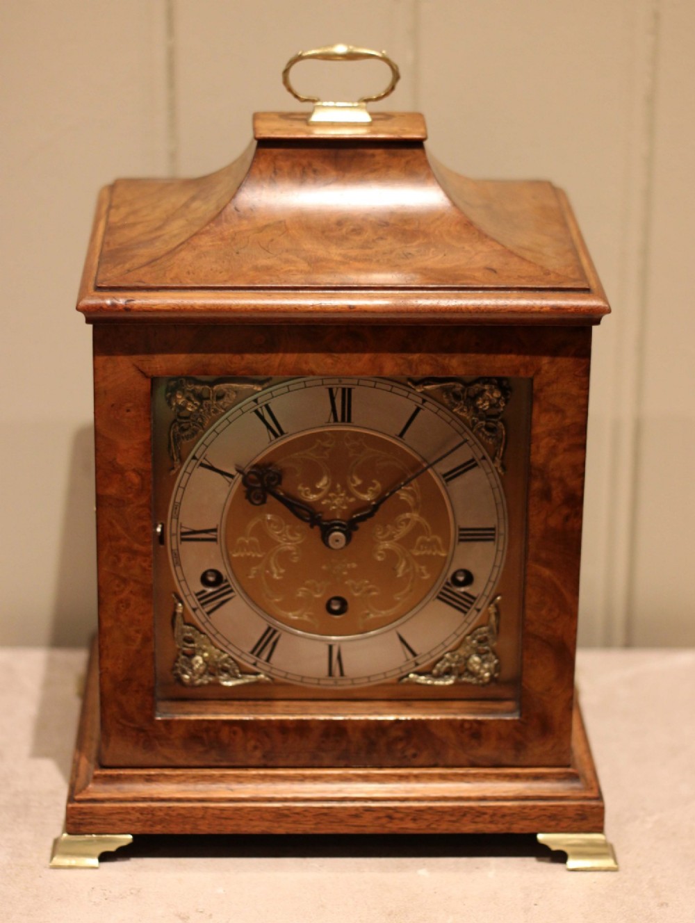 A burr walnut bracket clock featuring a caddy top with a brass carry handle, an ornate brass dial with a silvered chapter ring, and brass bracket feet. View XI