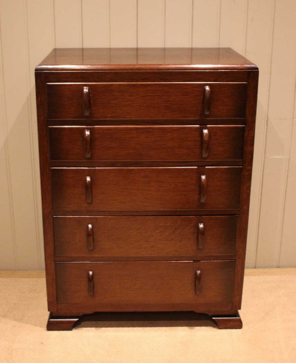 A dark brown oak Art Deco chest of drawers featuring five stacked drawers with matching wood handles and stepped feet.