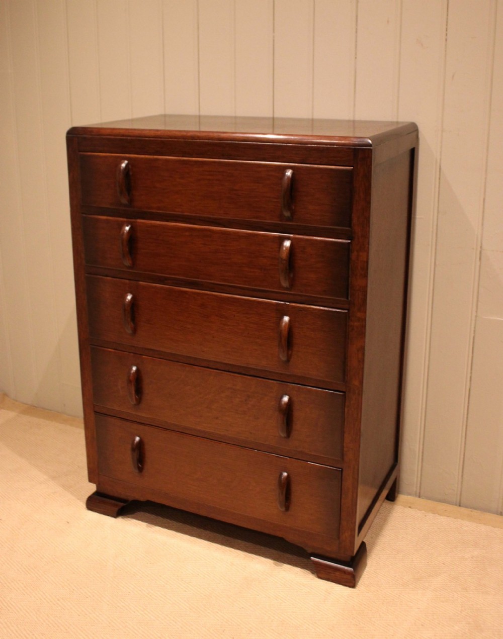 A dark brown oak Art Deco chest of drawers featuring five stacked drawers with matching wood handles and stepped feet. View III