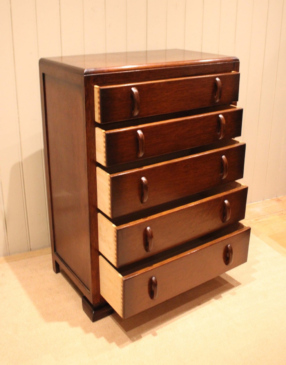 A dark brown oak Art Deco chest of drawers featuring five stacked drawers with matching wood handles and stepped feet. View V