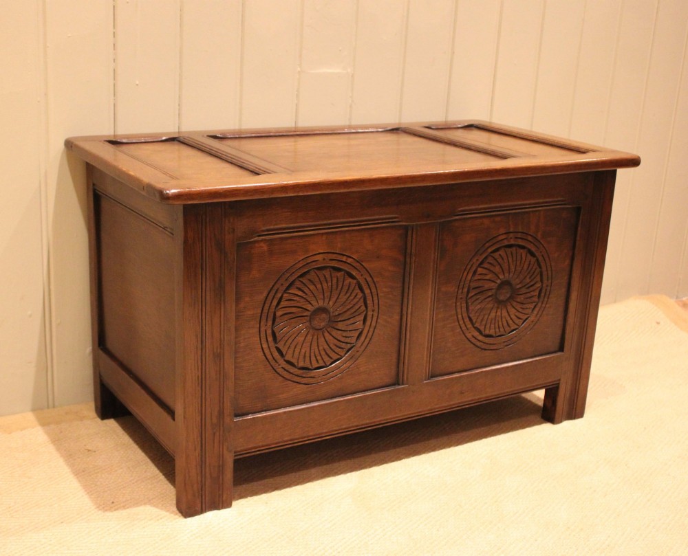A dark brown carved oak coffer featuring a three-panel lid and two front panels carved with circular rosette motifs. View V