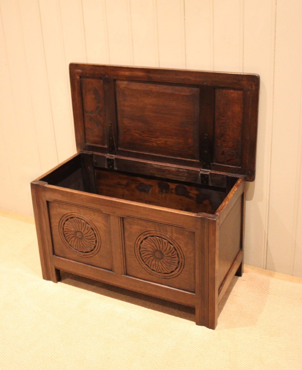A dark brown carved oak coffer featuring a three-panel lid and two front panels carved with circular rosette motifs. View VI