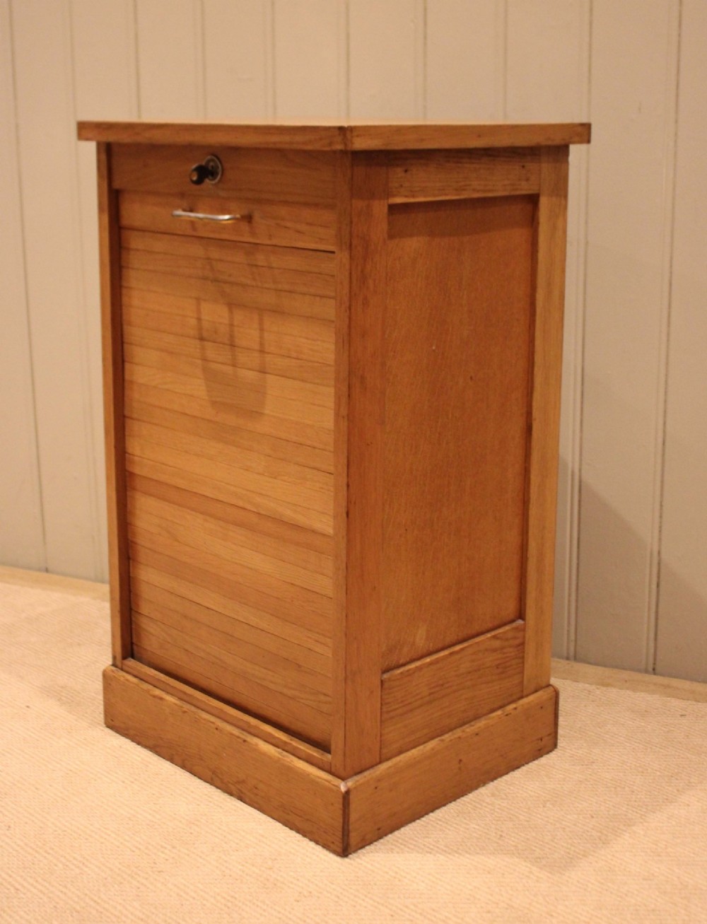 A small light oak filing cabinet featuring a slatted wooden tambour front with a metal handle and keyhole lock at the top.