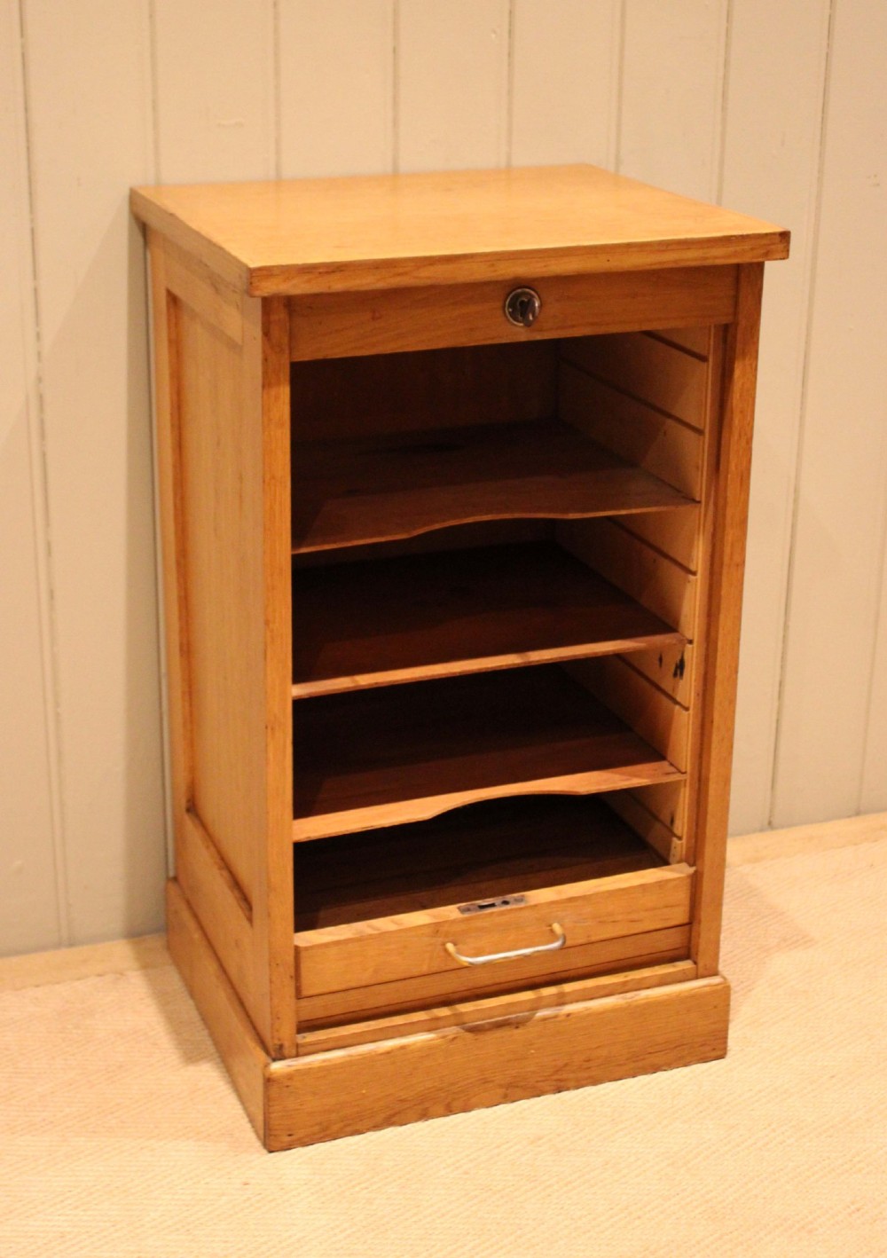 A small light oak filing cabinet featuring a slatted wooden tambour front with a metal handle and keyhole lock at the top. View II