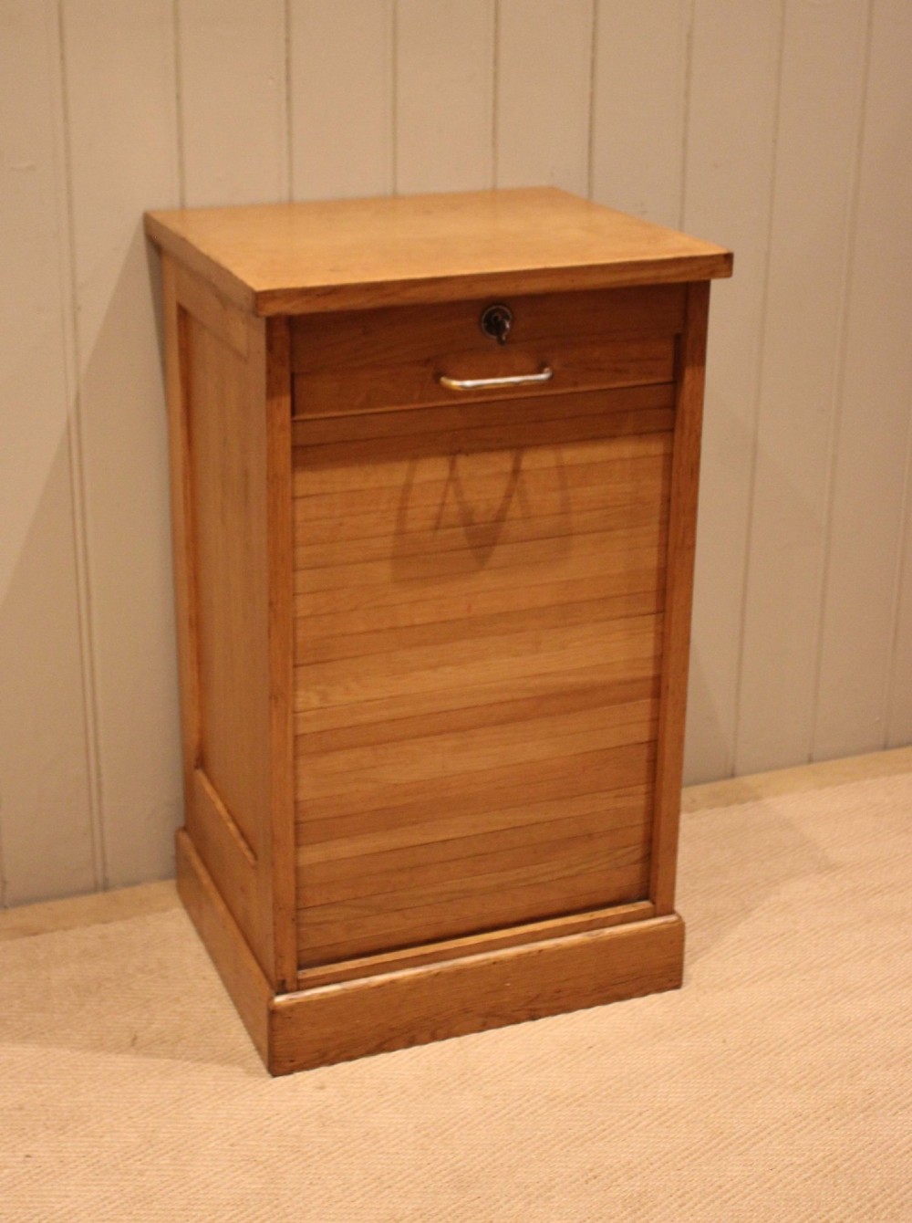 A small light oak filing cabinet featuring a slatted wooden tambour front with a metal handle and keyhole lock at the top. View III