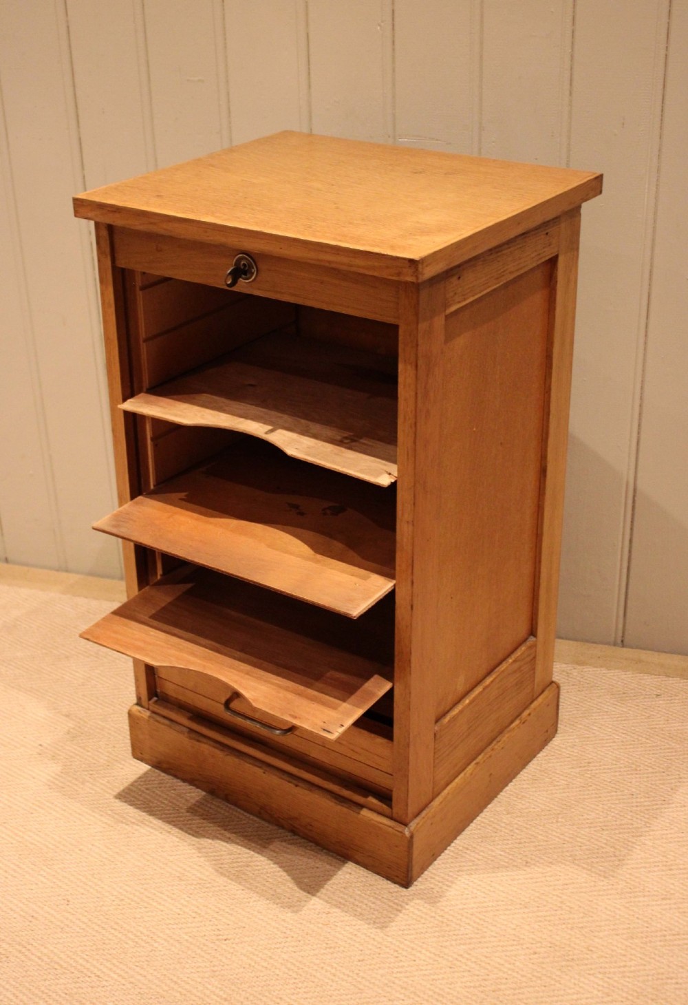 A small light oak filing cabinet featuring a slatted wooden tambour front with a metal handle and keyhole lock at the top. View IV