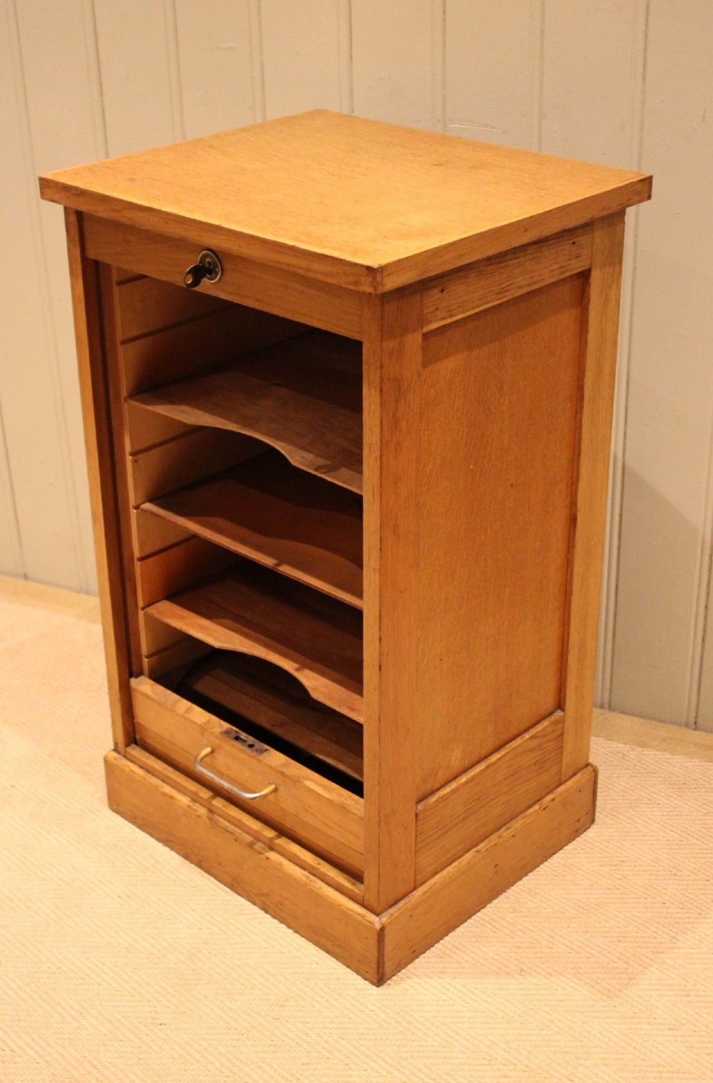 A small light oak filing cabinet featuring a slatted wooden tambour front with a metal handle and keyhole lock at the top. View VI