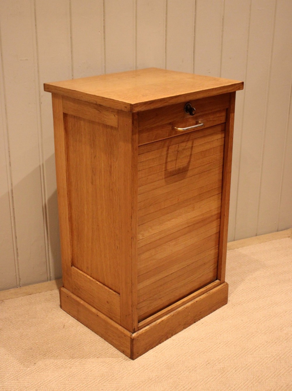 A small light oak filing cabinet featuring a slatted wooden tambour front with a metal handle and keyhole lock at the top. View VII