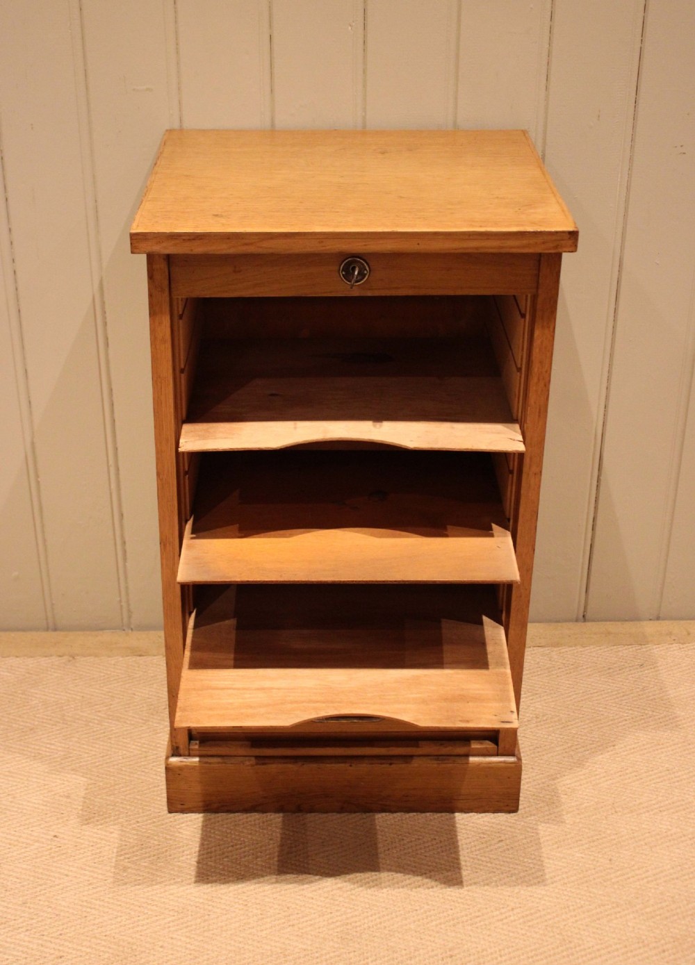 A small light oak filing cabinet featuring a slatted wooden tambour front with a metal handle and keyhole lock at the top. View IX