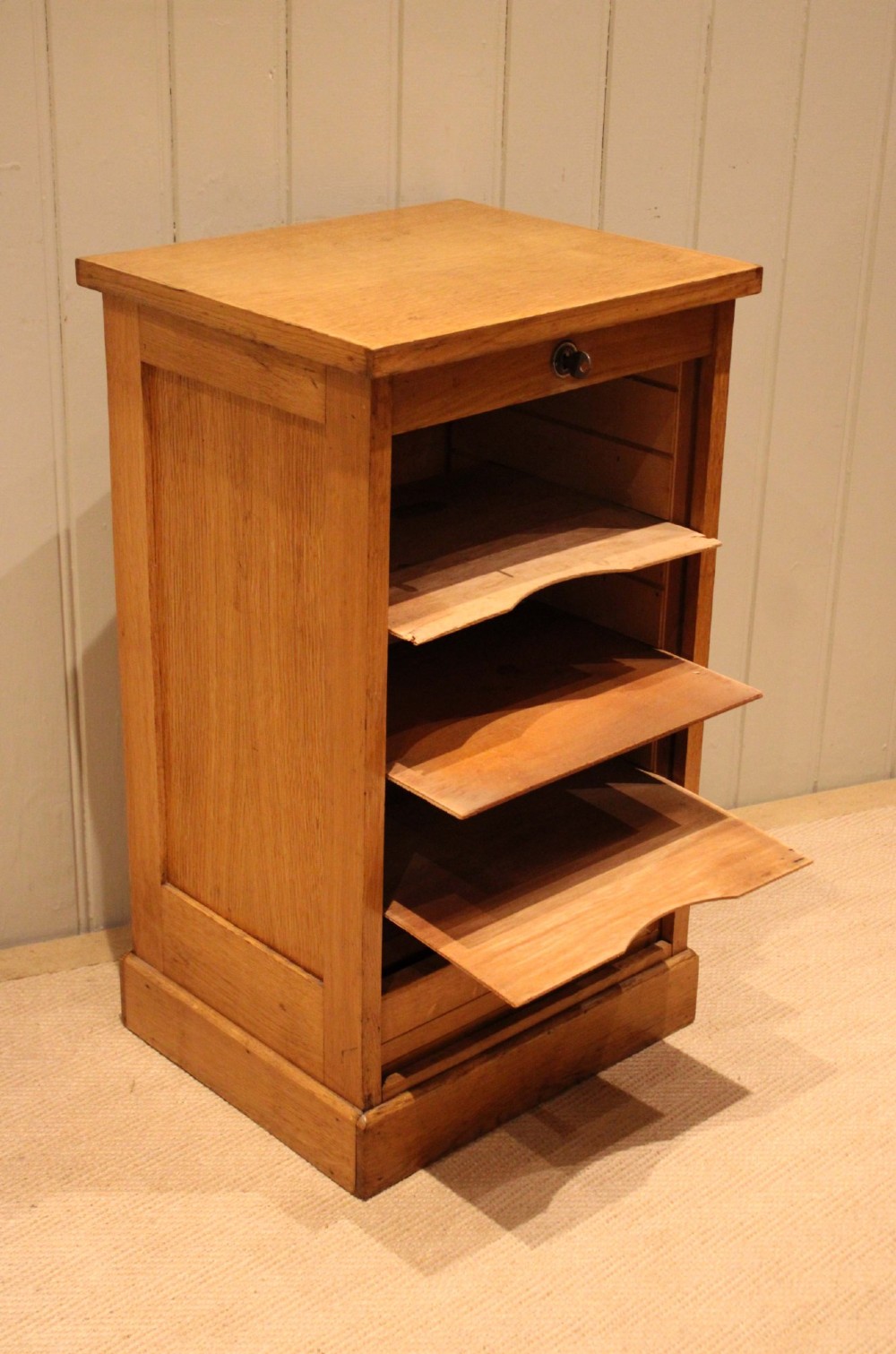 A small light oak filing cabinet featuring a slatted wooden tambour front with a metal handle and keyhole lock at the top. View X