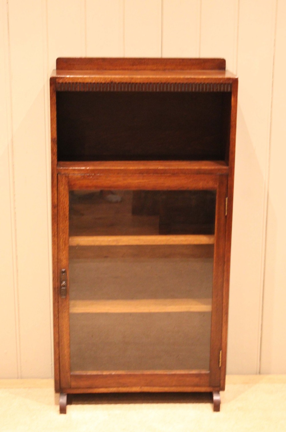 A medium oak freestanding bookcase featuring an open top compartment above a single glass-fronted door with internal shelving. View II