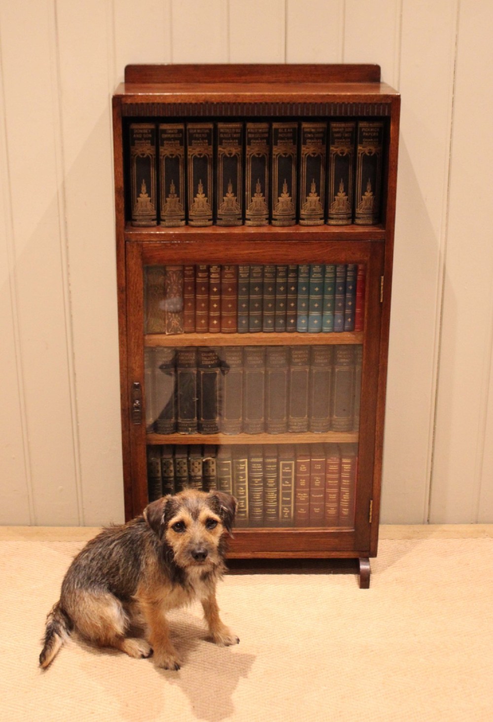 A medium oak freestanding bookcase featuring an open top compartment above a single glass-fronted door with internal shelving. View V