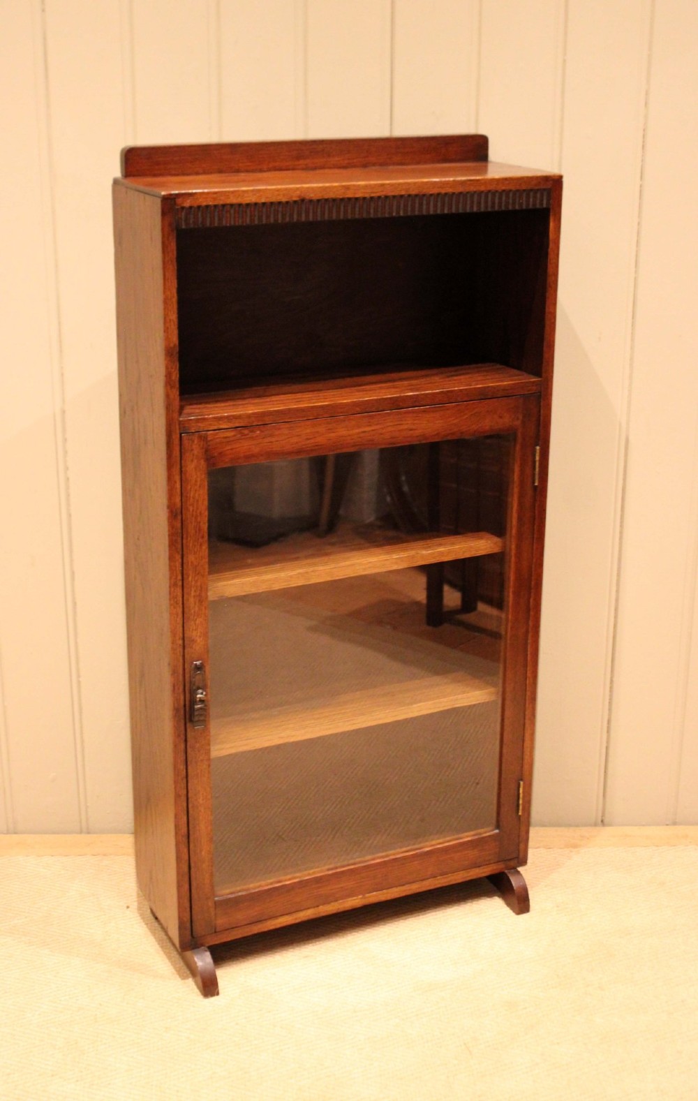 A medium oak freestanding bookcase featuring an open top compartment above a single glass-fronted door with internal shelving. View VIII