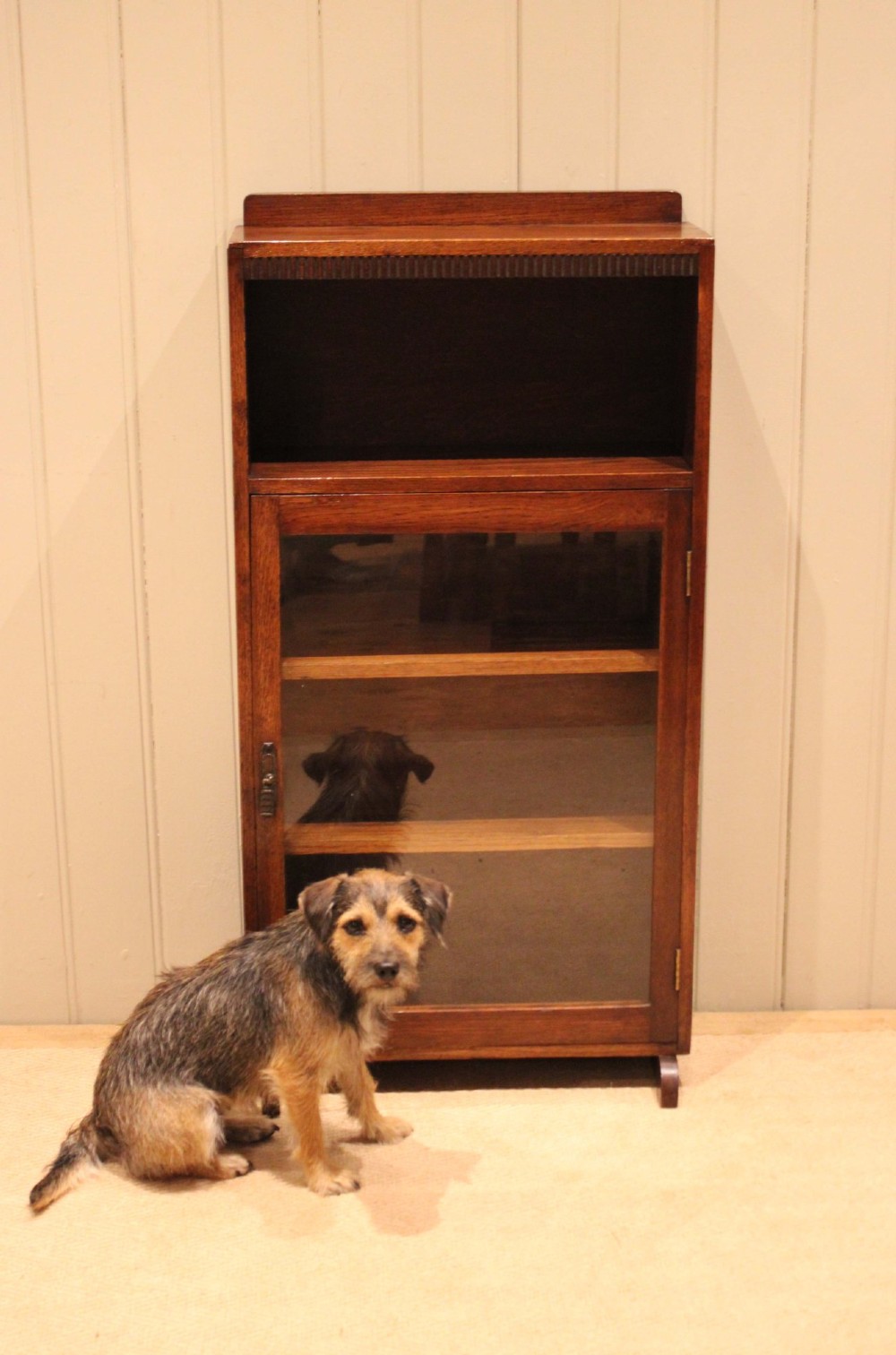 A medium oak freestanding bookcase featuring an open top compartment above a single glass-fronted door with internal shelving. View X