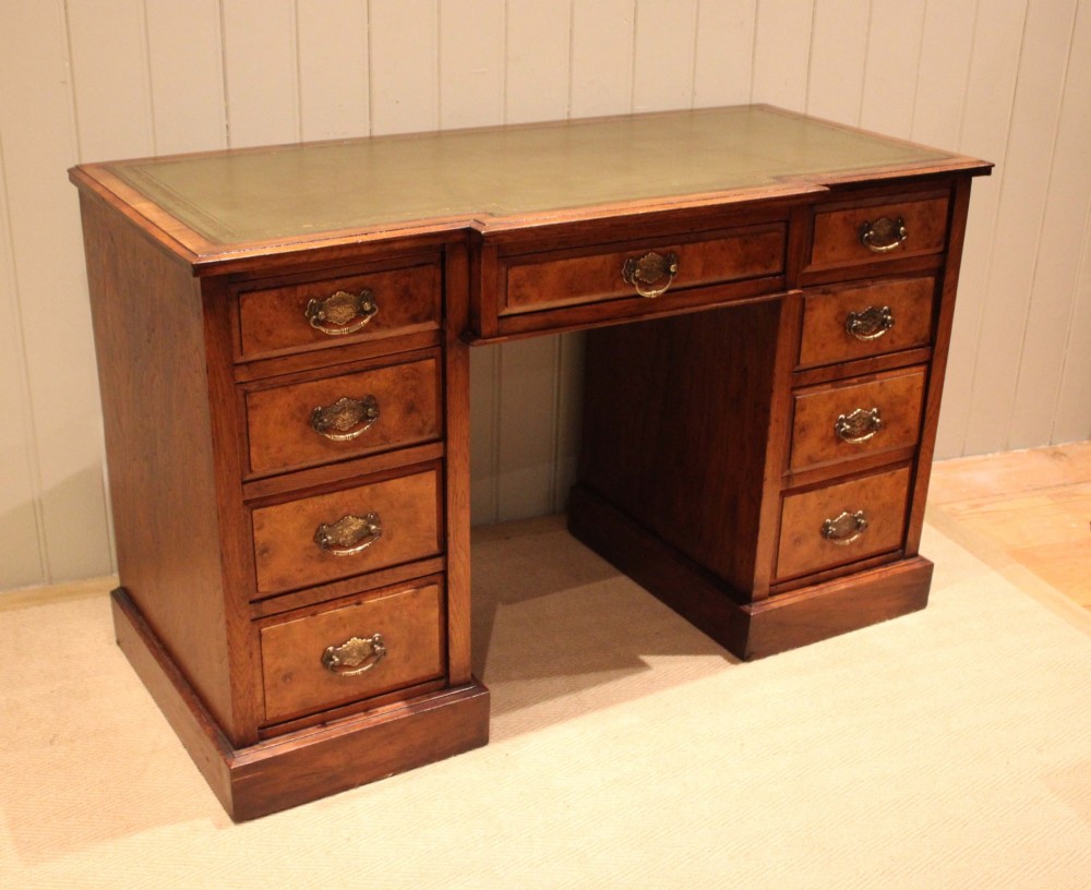 A walnut breakfront pedestal desk featuring nine drawers with brass handles and a green leather writing insert set into the top surface.