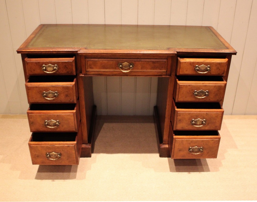 A walnut breakfront pedestal desk featuring nine drawers with brass handles and a green leather writing insert set into the top surface. View III