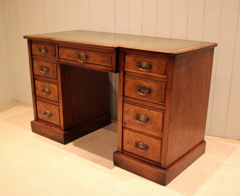 A walnut breakfront pedestal desk featuring nine drawers with brass handles and a green leather writing insert set into the top surface. View IV