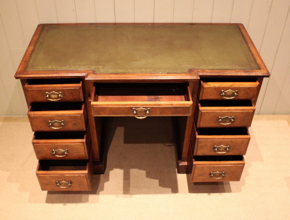 A walnut breakfront pedestal desk featuring nine drawers with brass handles and a green leather writing insert set into the top surface. View V