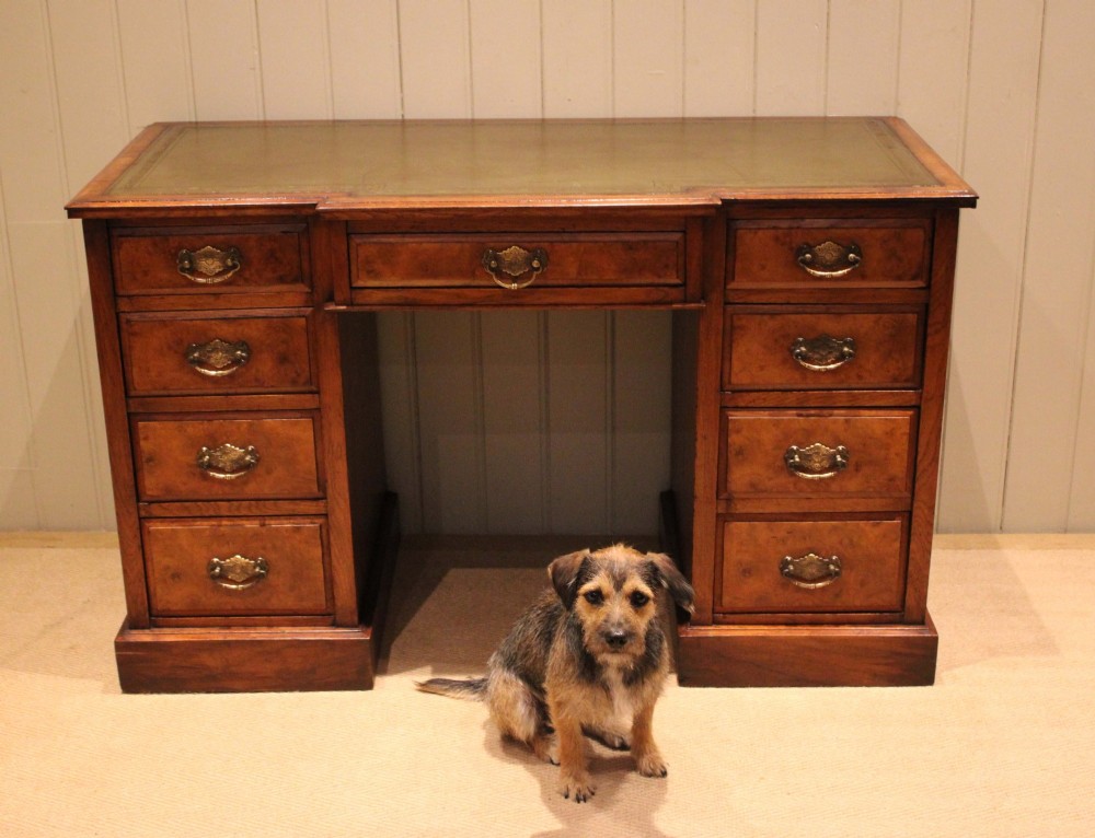 A walnut breakfront pedestal desk featuring nine drawers with brass handles and a green leather writing insert set into the top surface. View VI