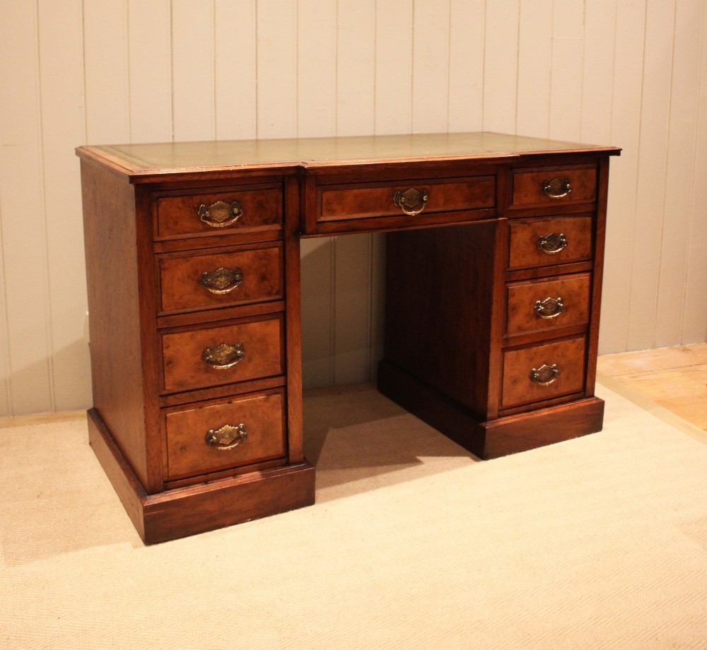 A walnut breakfront pedestal desk featuring nine drawers with brass handles and a green leather writing insert set into the top surface. View VII