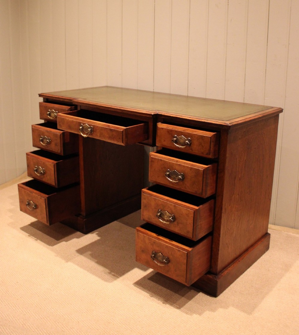 A walnut breakfront pedestal desk featuring nine drawers with brass handles and a green leather writing insert set into the top surface. View VIII