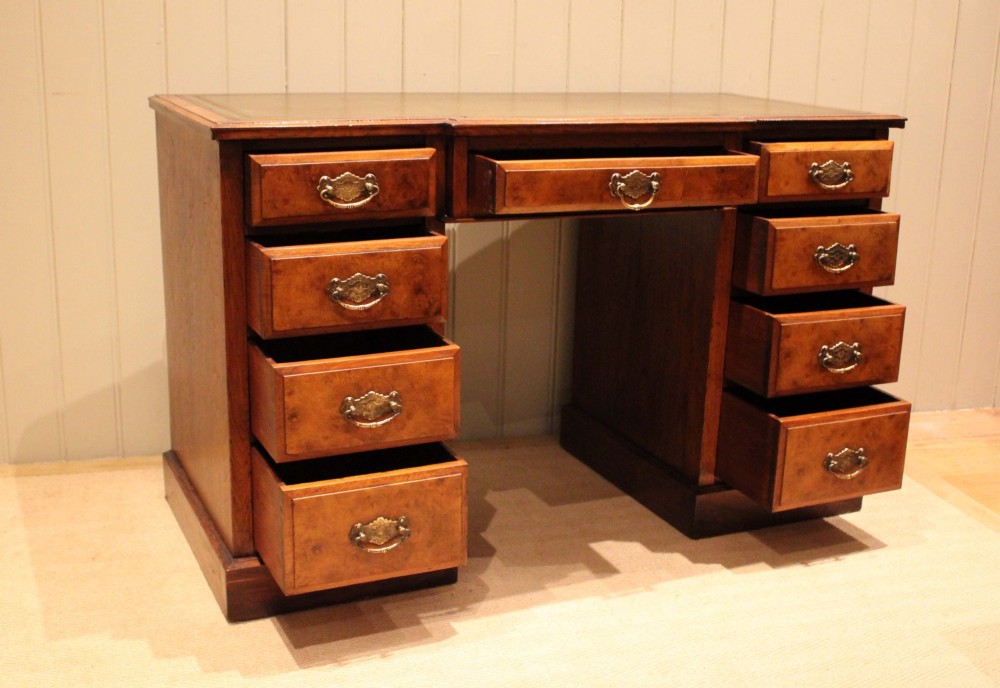 A walnut breakfront pedestal desk featuring nine drawers with brass handles and a green leather writing insert set into the top surface. View IX