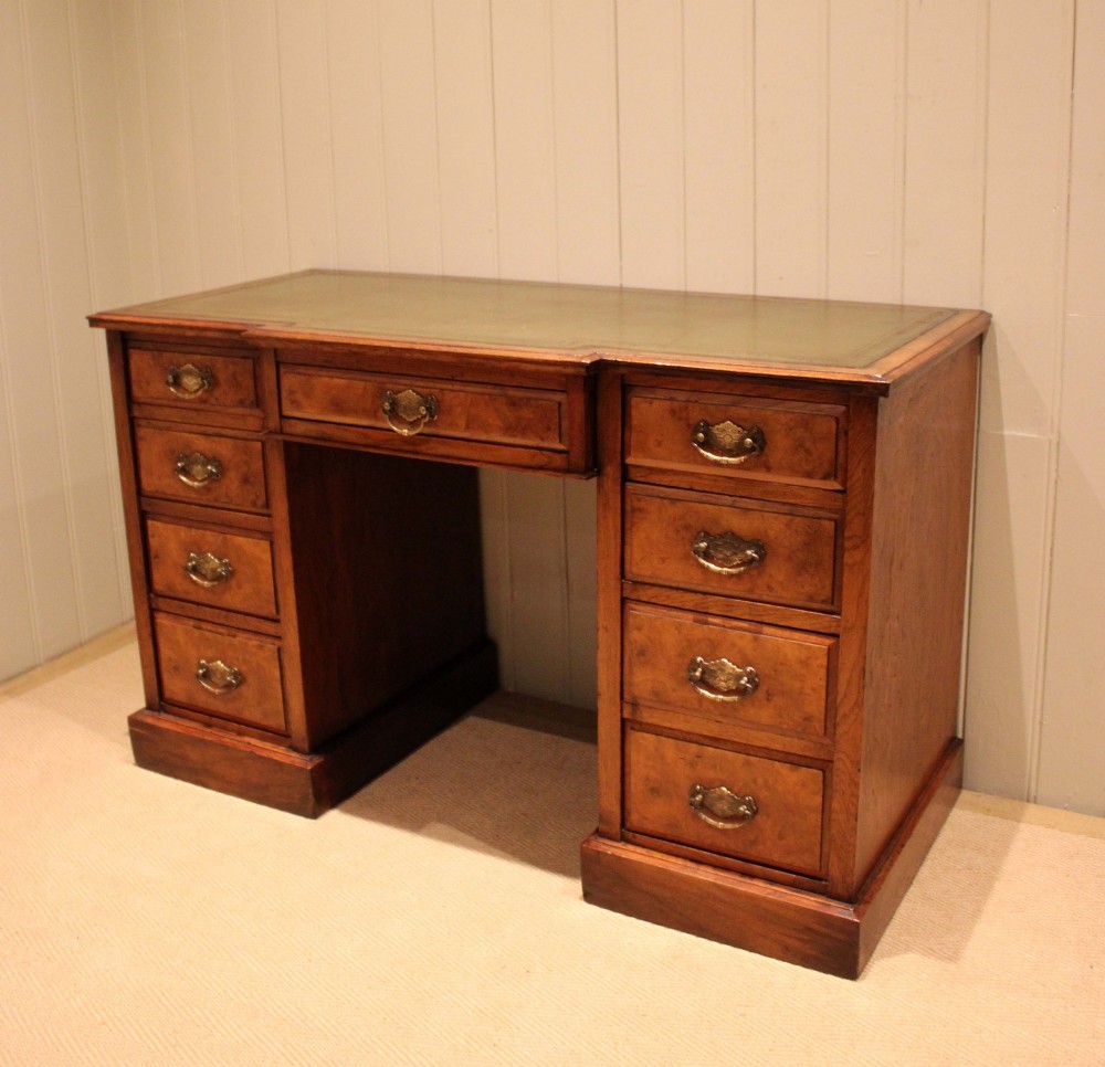 A walnut breakfront pedestal desk featuring nine drawers with brass handles and a green leather writing insert set into the top surface. View X