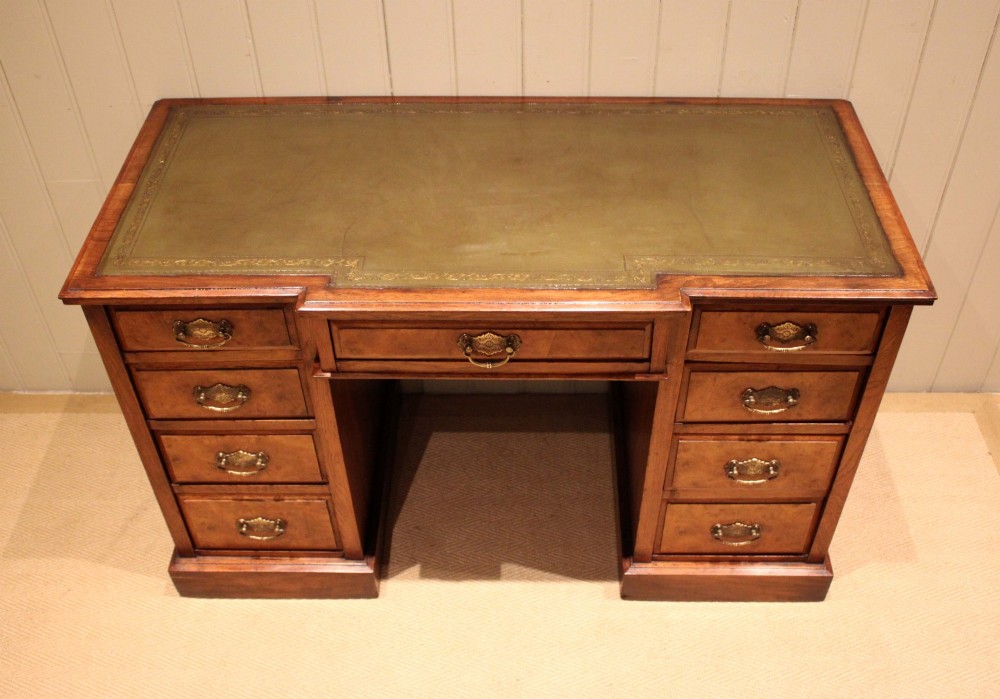 A walnut breakfront pedestal desk featuring nine drawers with brass handles and a green leather writing insert set into the top surface. View XI