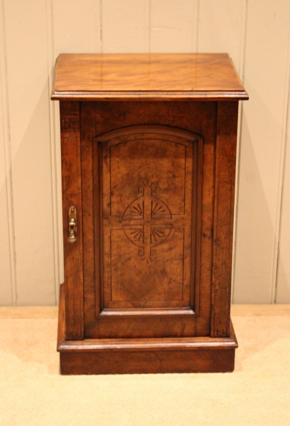 A late 19th-century walnut bedside cabinet featuring a single door with incised geometric detail, a brass drop handle, and a solid plinth base. View II