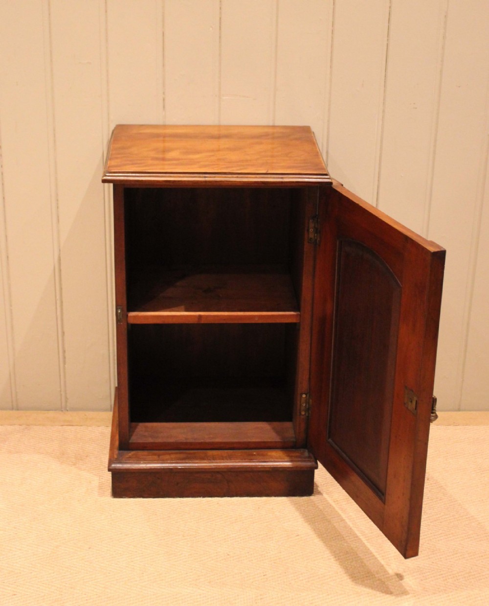 A late 19th-century walnut bedside cabinet featuring a single door with incised geometric detail, a brass drop handle, and a solid plinth base. View VI