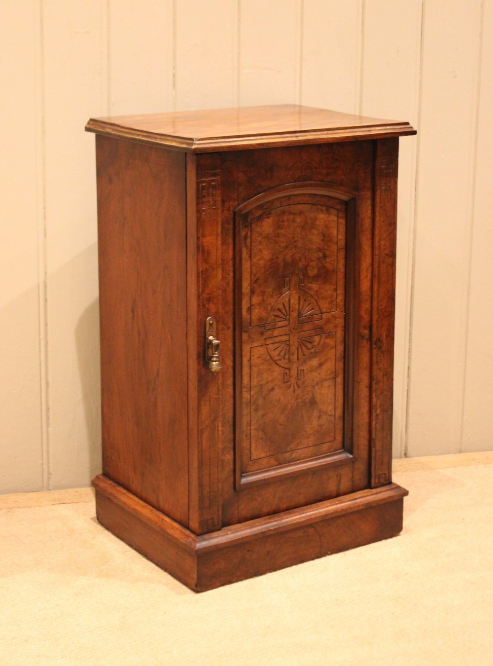A late 19th-century walnut bedside cabinet featuring a single door with incised geometric detail, a brass drop handle, and a solid plinth base. View VII
