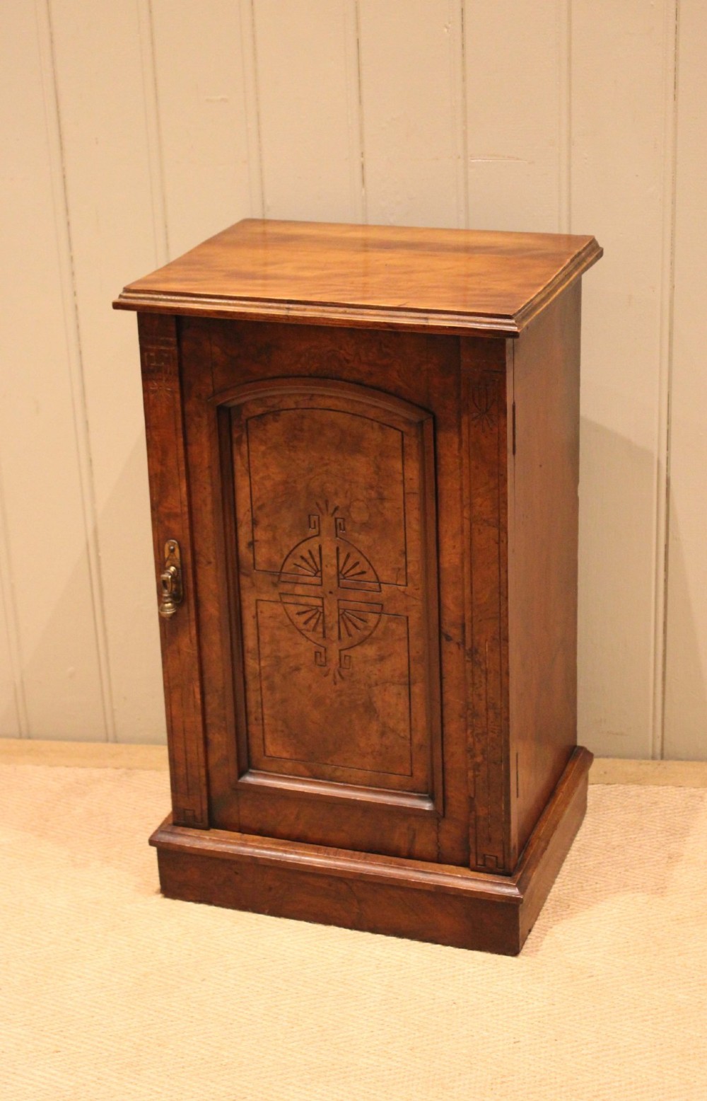 A late 19th-century walnut bedside cabinet featuring a single door with incised geometric detail, a brass drop handle, and a solid plinth base. View VIII